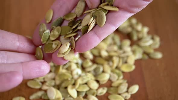A Lot of Raw Pumpkin Seeds Fall From Female Hands on the Table alt