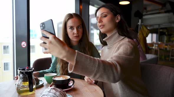 Two Young Attractive Girls in a Cafe Take Selfies Smile and Pose