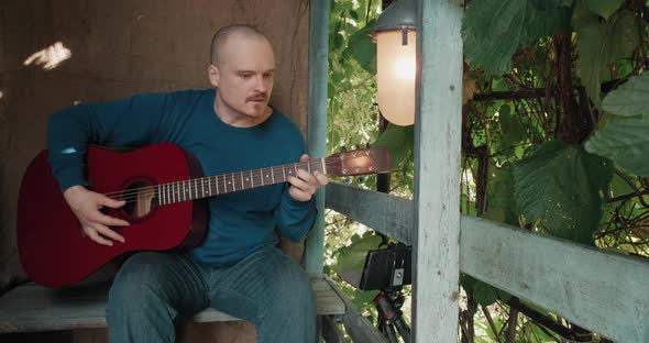 Man is Sitting on Porch of House and Taking Online Lessons on Acoustic Guitar