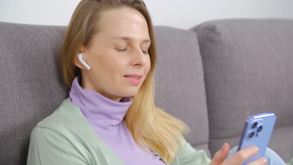 Happy woman typing message on mobile phone and listening to music in wireless headphones in 4k video alt