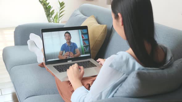 Woman Greeting With Colleagues In Video Conference From Laptop At Home Living Room alt