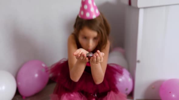 Beautiful little girl blows up multicolored confetti, having fun at home birthday party alt