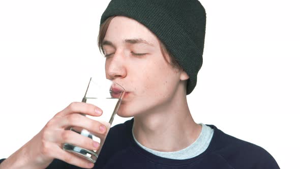 Portrait of Blueeyed Male Teenager with Clean Skin in Sweatshirt and Hat Drinking Still Water From alt