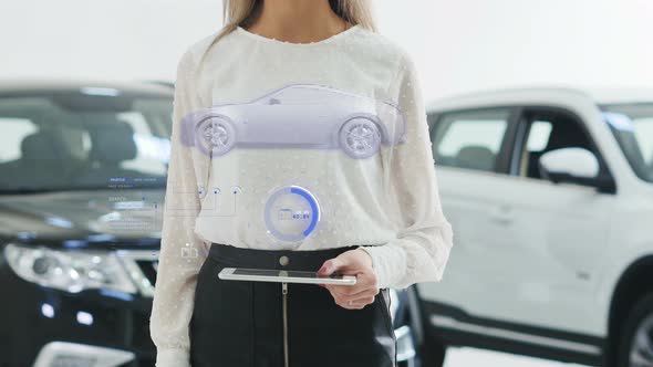 Girl Car Salesman Holding a Tablet. The Tablet Appears Hologram 3D Car with HUD Elements