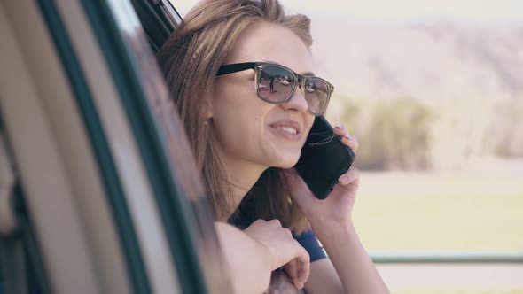 Young Lady Talks on Phone Leaning Out Car Window at Field alt