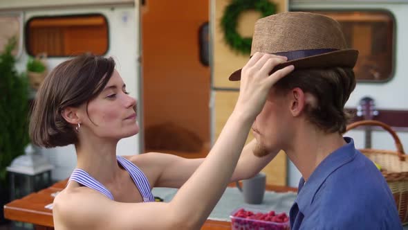 Cute Couple Man and Woman Having Fun Together at Wooden Table Outdoors Girl Putting Her Hat on a Man alt