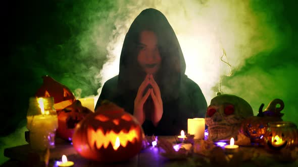 Young Witch in Halloween Decorations Surrounded By Fume Sits Holding Hands Together Like Praying alt
