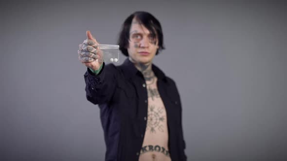 Closeup White Pills Drugs in Pack with Blurred Smiling Tattooed Young Man at Grey Background alt