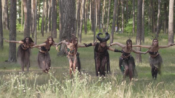 Young Women in Theatrical Costumes of Forest Dwellers or Devils Dancing in Forest alt