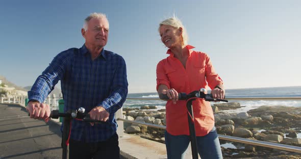 Senior couple walking next to electronic scooter alongside beach alt