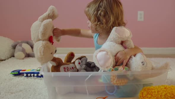 Little Girl Playing with Stuffed Animals While Sitting Inside Plastic Bin  alt