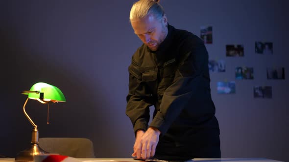 Focused Ukrainian Police Officer Opening Case Folder Examining Photos Indoors alt