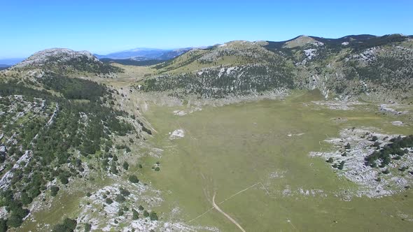 Flying above thick forest of Dinara mountain with grass plains in between alt