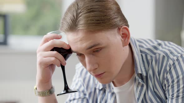Closeup Portrait of Sad Frustrated Young Man Holding Glass with Red Wine at Forehead Looking at alt