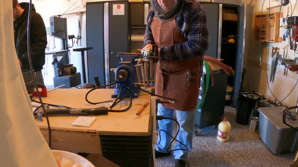 Two men working in a home garage metal shop - using an angle grinder to cut steel in slow motion alt