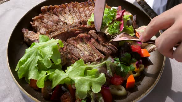 Man Hand with Fork and Knife Take Portion of Fresh Roasted Tbone Beef Steak alt