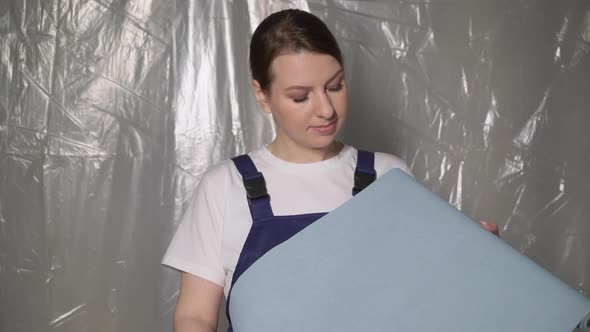 Woman Builder in Blue Overalls with Roll of Blue Wallpaper