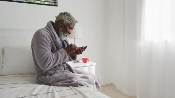Senior man using smartphone while sitting on bed at home alt