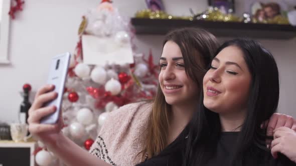 Young Multiethnic Women Sitting By Christmas Tree and Taking Selfies