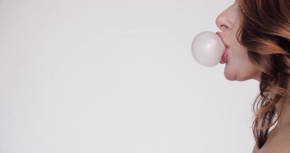 Side View of Young Woman Blowing Pink Bubble Gum