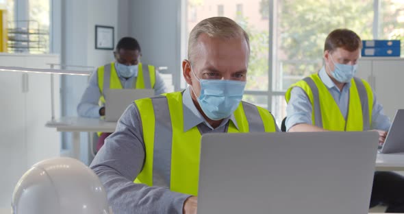 Diverse Engineers in Safety Mask Working on Laptop in Open Space Office alt