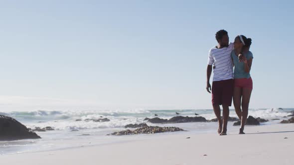 African american couple smiling, embracing and walking on the beach alt