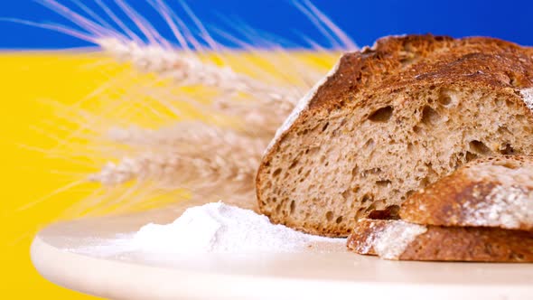 A Loaf of Bread and Cut Slices Rye Ears on Wooden Tableon the Background of the Ukrainian Flag