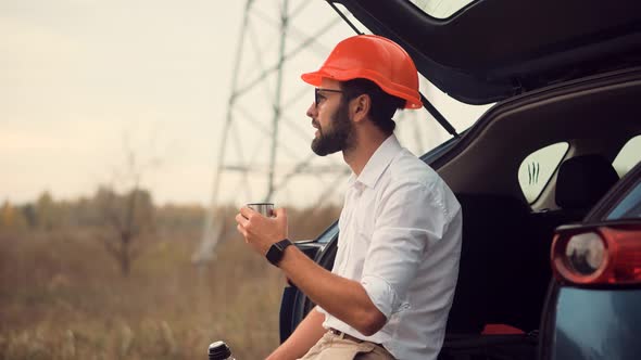 Electrical Engineer In Hard Hat On Power Lines.Investor Engineer With Hardhat Drinking Tea alt