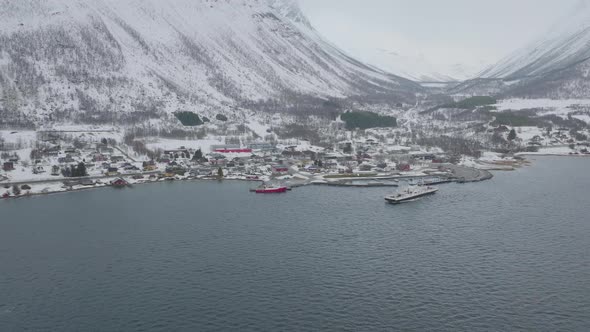 Boat departs snow covered Olderdalen ferry pier, arctic winter aerial view alt