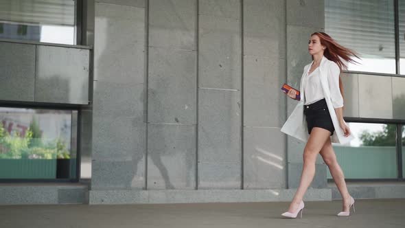 Beautiful confident business woman with red hair in fashion clothes walk to work near office. alt