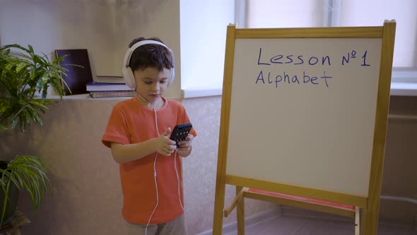 A Boy in White Headphones is Studying Online Listening to a Teacher's Lecture