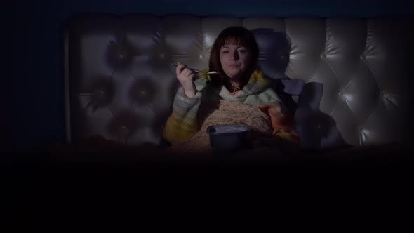Woman Sitting on the Bed in the Evening Watching Tv and Eating Ice Cream
