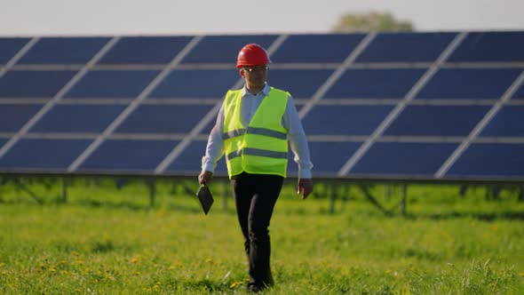 Industrial Man Engineer in Uniform Walking Through Solar Panel Field for Examination