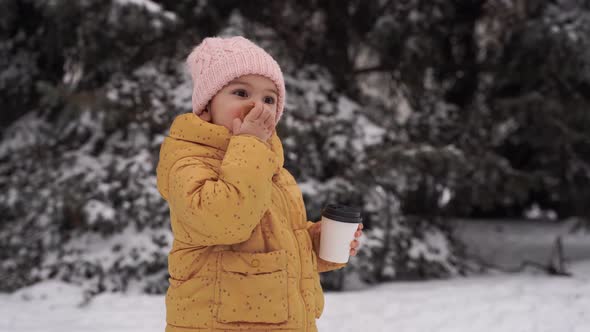 Child Girl Drinking Cocoa and Eating Cookie Outdoors in Winter Snowy Day alt