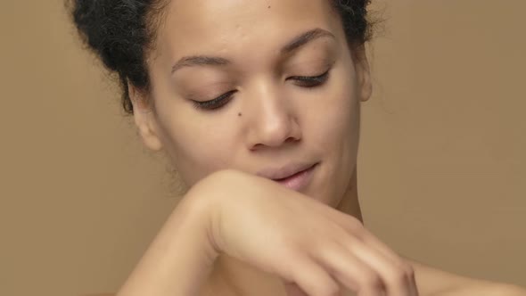 Beauty Portrait of Young African American Woman Twisting Off a Jar of Cream and Enjoying Its Aroma alt