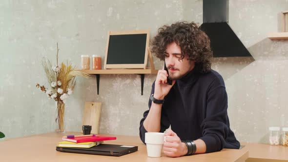 Man on Kitchen is Smiling Drinking Coffee and Talking on the Phone alt