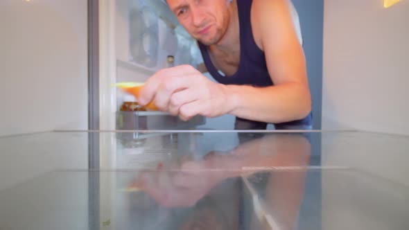 man looks into an empty refrigerator and takes out bottle of alcohol. Alcoholism alt