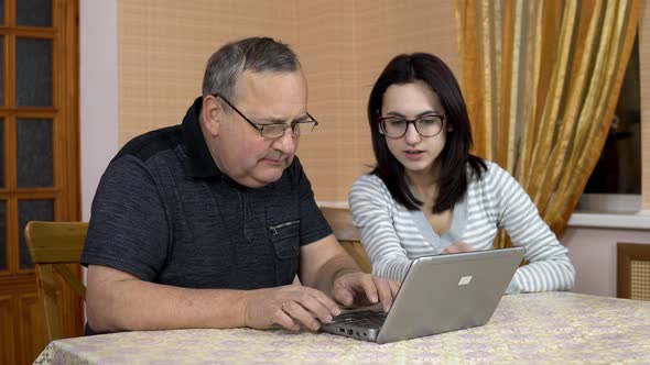 Daughter Teaches Father How To Use a Laptop. A Young Woman Shows Her Old Father Where To Click in a alt