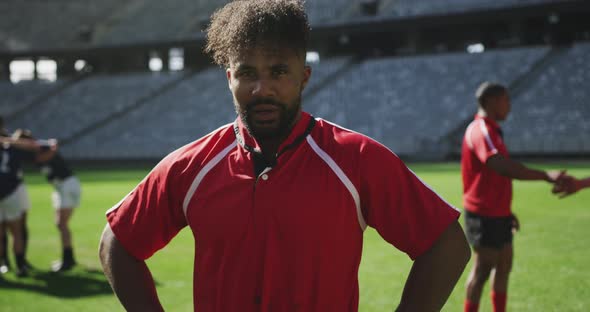 Male rugby player standing with hands on hip in stadium alt