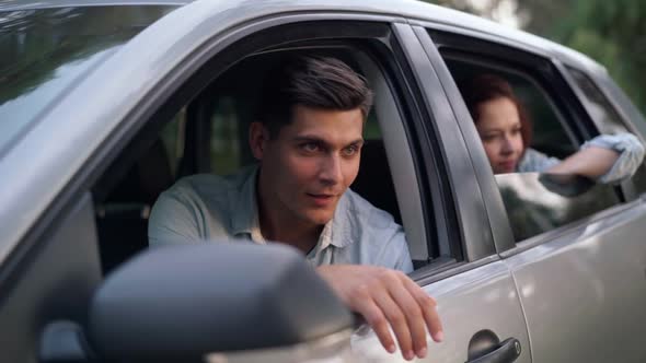 Smiling Handsome Man Sitting on Driver's Seat Talking with Blurred Beautiful Woman on Back Seat alt