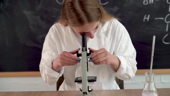 Concentrated Biologist Millennial Girl Teacher in a White Coat in the Office with a Blackboard Looks alt