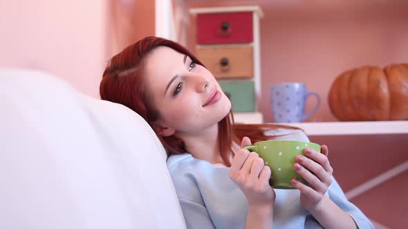 Redhead girl cup sitting on sofa at home