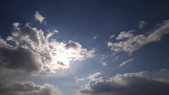 Beautiful time lapse. Sun rays break through white fluffy clouds on vivid blue sky alt