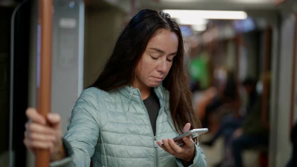 Adult Woman in Underground Holding Handrails and Viewing Social Networking By Mobile Phone alt