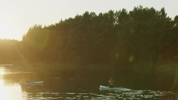 Couple of Surfers in Lake Woman Lying on Surfing Board and Man Paddling to Her People Sunbathing on alt