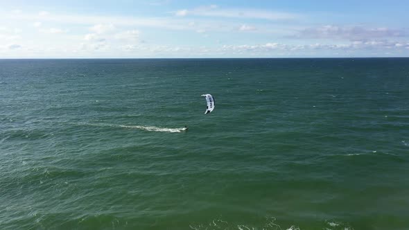 AERIAL: Locked Shot of Surfer Passing By with Power Kite Alongside Blue Sky in Background