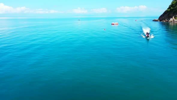 Fishing boat sailing on calm azure lagoon alongside beautiful shore of tropical island with rocky co alt