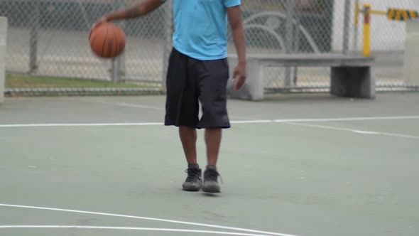 Young man basketball player dribbling a basketball on an outdoor court. alt