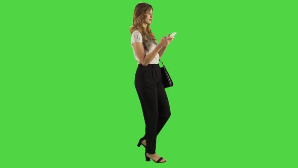 Texting while walking by a young businesswoman over a green screen. 4K alt