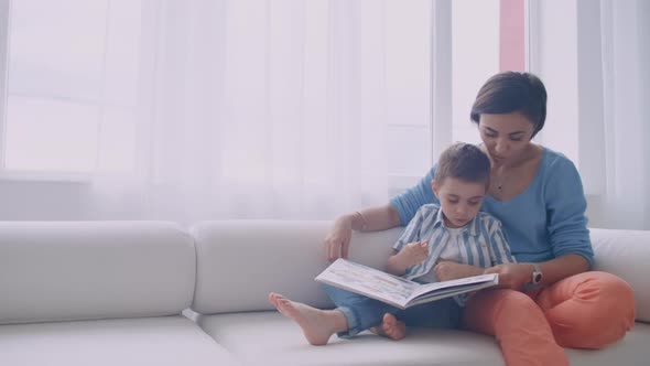 Happy Mother and Child Son Reading Book Laughing in Bed alt